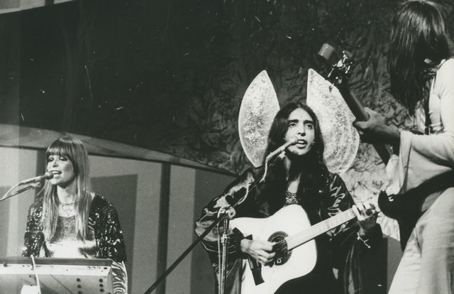 A imagem apresenta Os Mutantes cantando e cada um em um estrumento musical